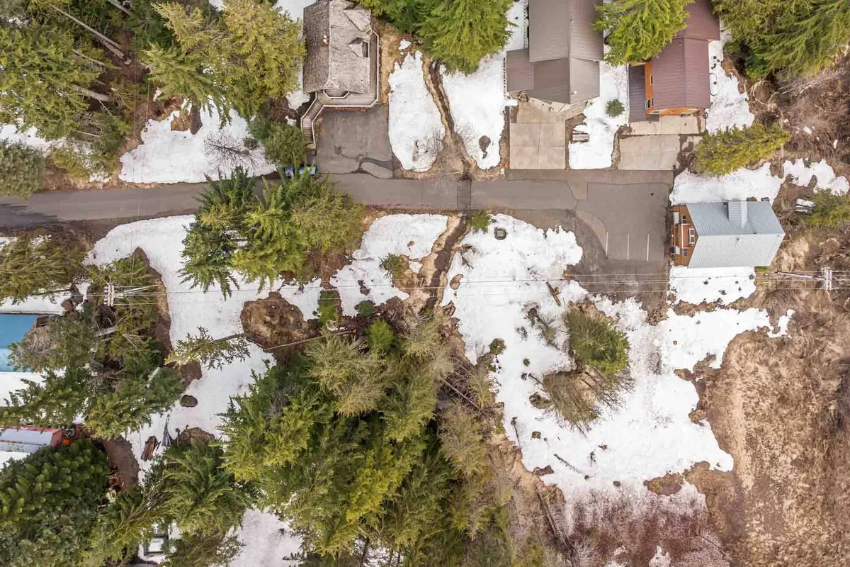 A peaceful neighborhood scene featuring residential homes nestled among snow-covered areas and green trees with a visible roadway. The environment feels tranquil and accessible, emphasizing a walkable, community-oriented village vibe.