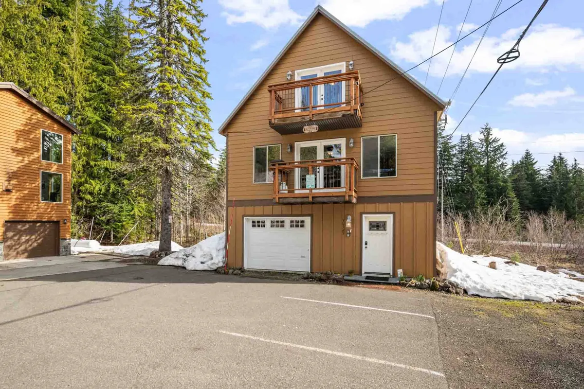 This exterior image showcases the chalet's welcoming wooden facade flanked by two balconies, surrounded by snowy trees and a driveway. The scene captures the home’s direct connection to the outdoors and hints at walkable access to the community.