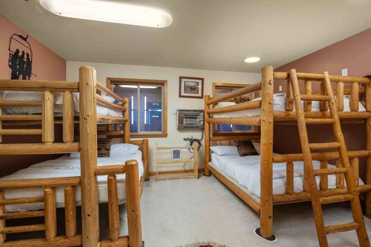 A cozy bunk room outfitted with sturdy wooden bunk beds and wall decorations. The communal design encourages group bonding and provides a playful, welcoming environment perfect for kids, teens, or friends.