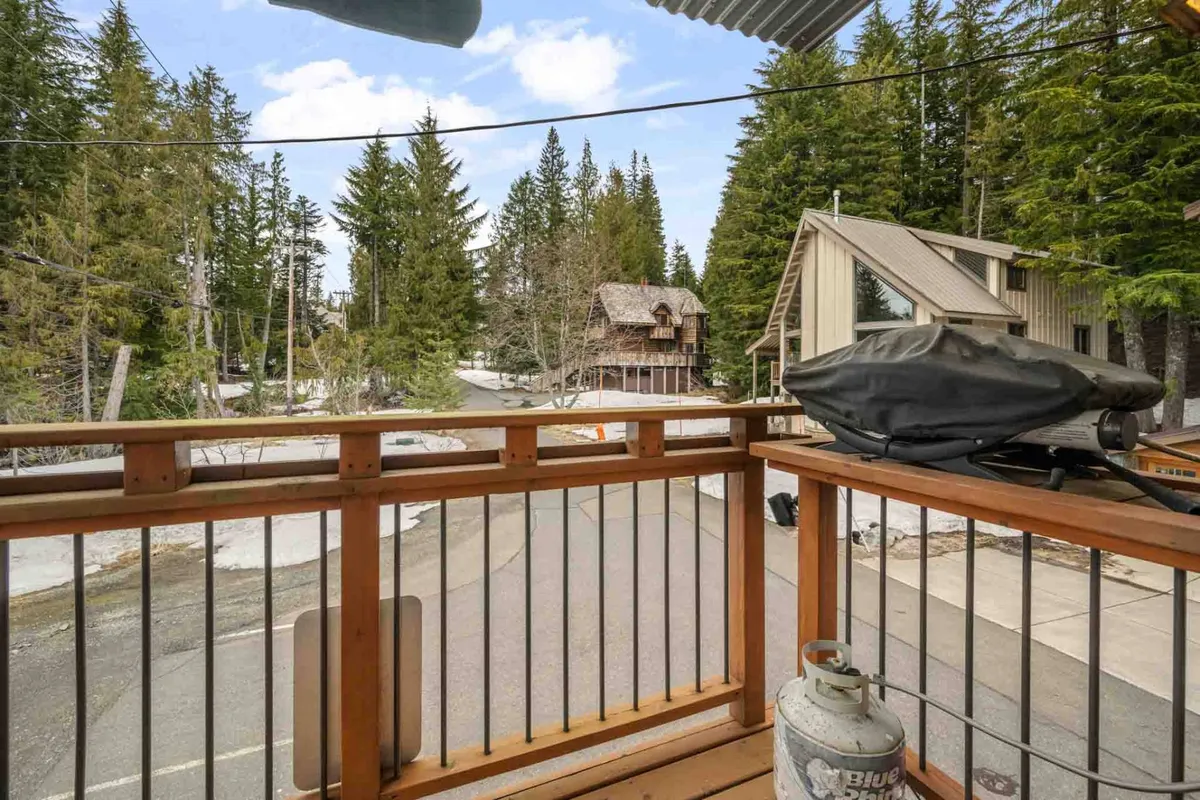 A peaceful exterior deck surrounded by trees, highlighted by a wooden railing and distant views of another cabin. The space evokes relaxation and connection with nature, ideal for outdoor breaks or gatherings. The deck is suitable for grilling or enjoying the mountain air.