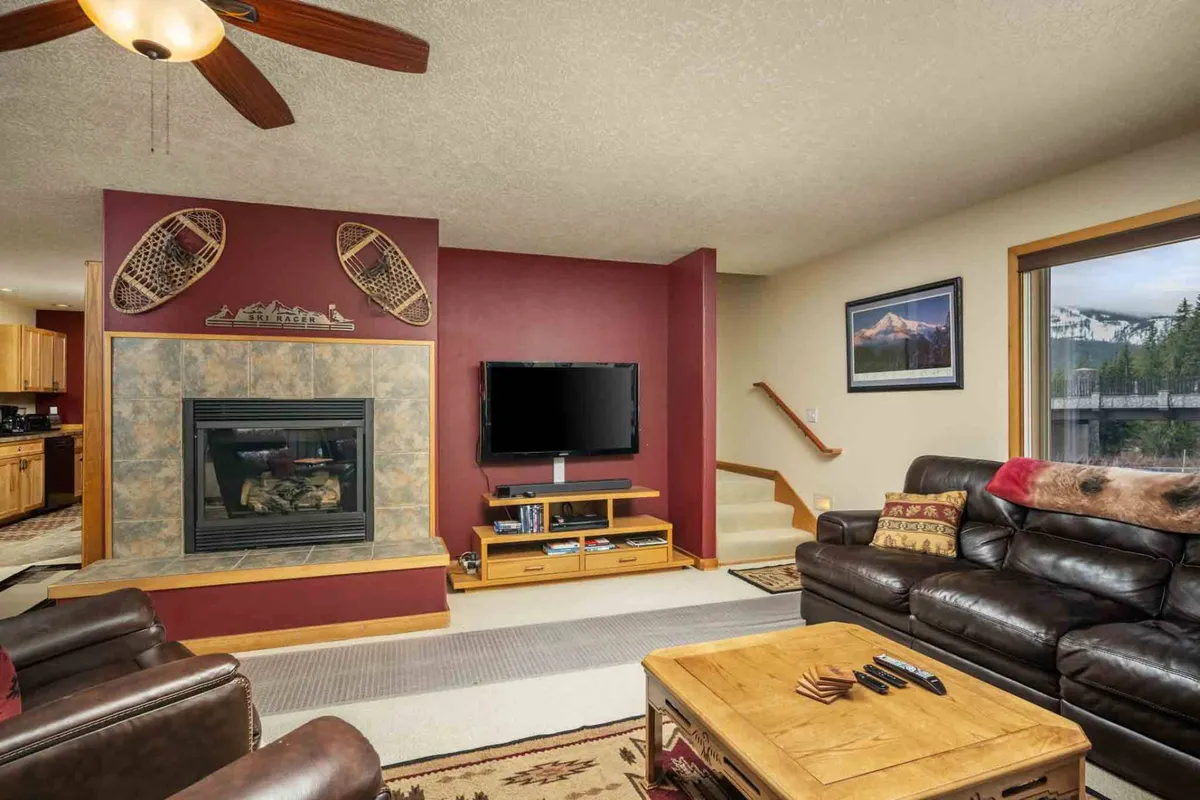 A close-up view of the living area, featuring a stone gas fireplace, a large comfortable sofa, a wooden coffee table, and a flat screen TV. The warm tones and inviting furnishings make it ideal for relaxing, watching movies, or sharing stories after a day outdoors.