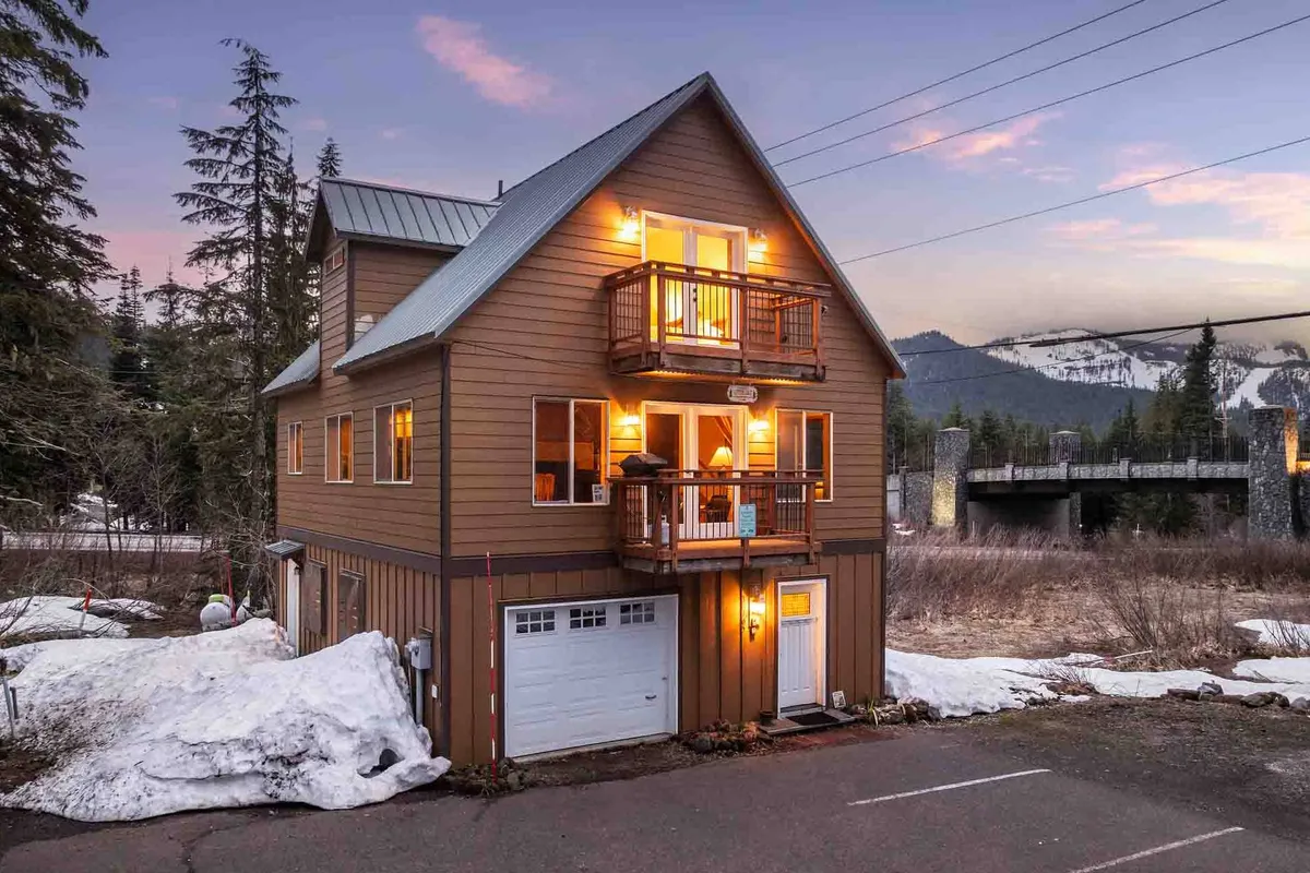 An inviting exterior view of the house with warm window glows, balconies, and a dramatic mountain backdrop. The scene conveys warmth, safety, and a welcoming environment, with hints at both interior comfort and exterior security.