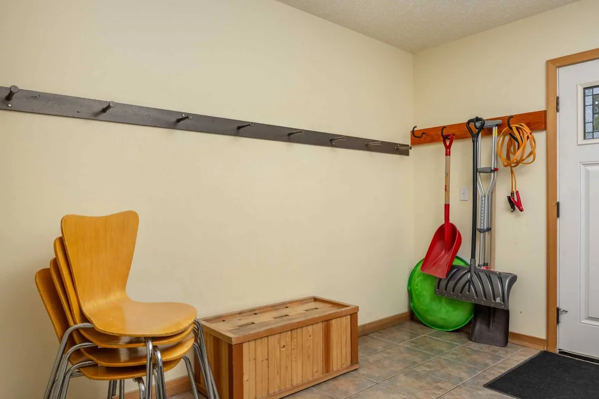 A functional mudroom scene featuring a wooden storage bench, a stack of chairs, and tools hanging on the wall. The layout emphasizes practicality and organization, suitable for handling outdoor gear, shoes, and seasonal equipment.