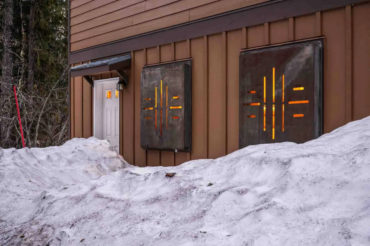 An inviting exterior shot featuring the home's entrance warmly illuminated on a snowy evening. The softly glowing lights and snow-covered ground create a welcoming, cozy atmosphere, hinting at the comfort and convenience awaiting returning adventurers.